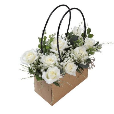 A bouquet of white roses in a brown paper bag with black handles.