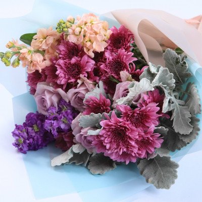 Bouquet with purple roses, chrysanthemums, and stock flowers in blue and pink wrapping.