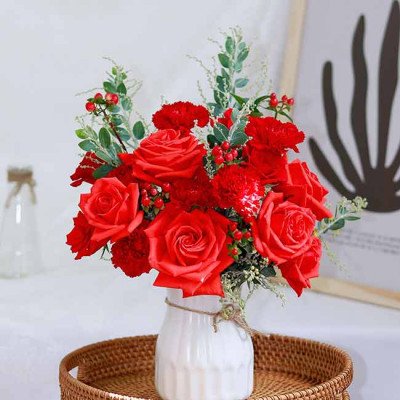 Red roses and carnations in a white vase tied with twine.
