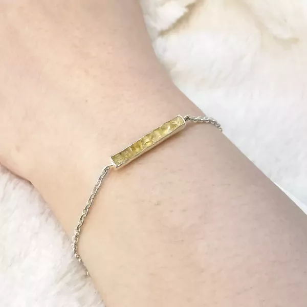 Silver chain bracelet with hammered gold bar charm on a wrist.