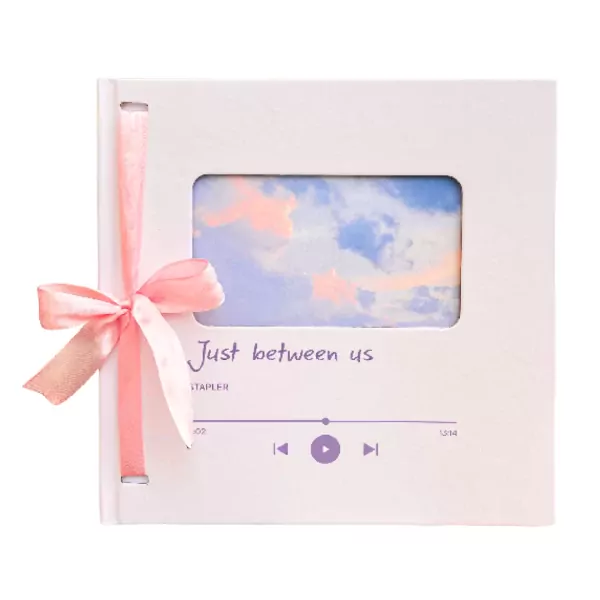 White notebook with pink ribbon, featuring a sky photo and "Just between us" text.