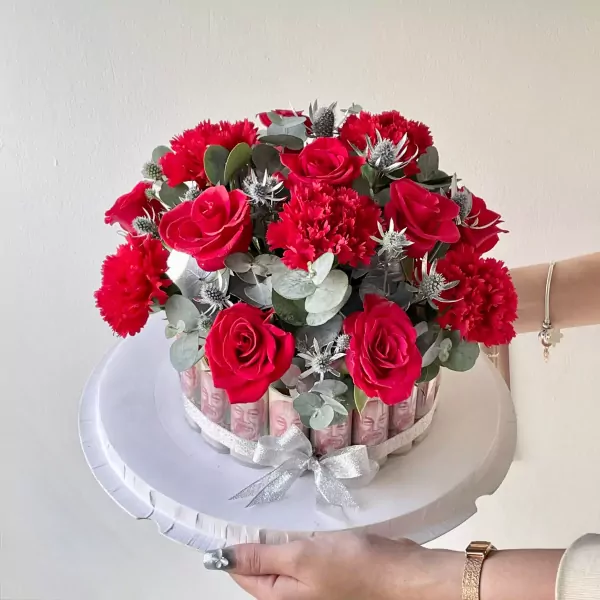 Red roses and carnations in a money cake arrangement with a silver bow.