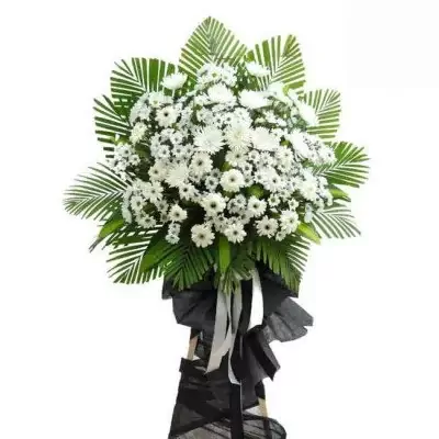 White flower arrangement with green leaves and black ribbon on a wooden stand.
