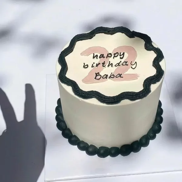 White cake with black frosting border, "happy birthday Baba" and "22" in pink.