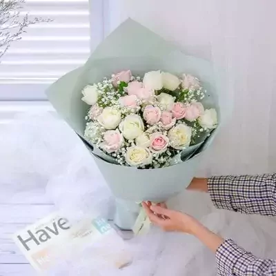 Pastel and white roses with baby's breath in light blue paper wrap, tied with ribbon.