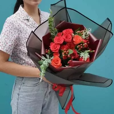 Person holding a red rose bouquet in black and maroon wrapping with red ribbon.