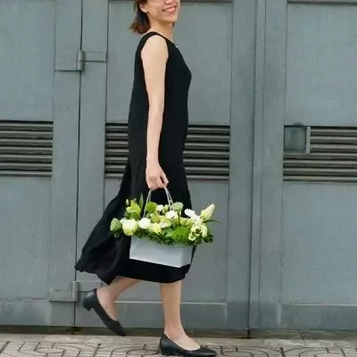 Woman in black dress carrying a basket of white and green flowers.
