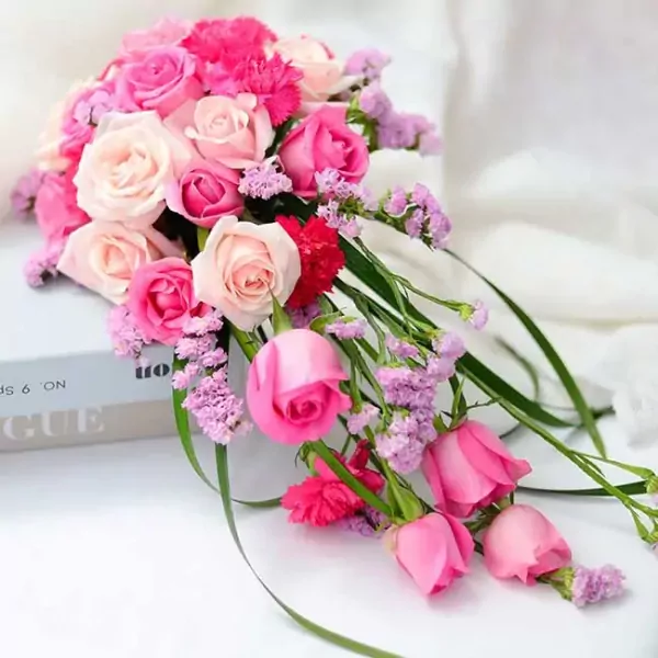 Pink and cream cascade wedding bouquet with roses and small purple flowers.