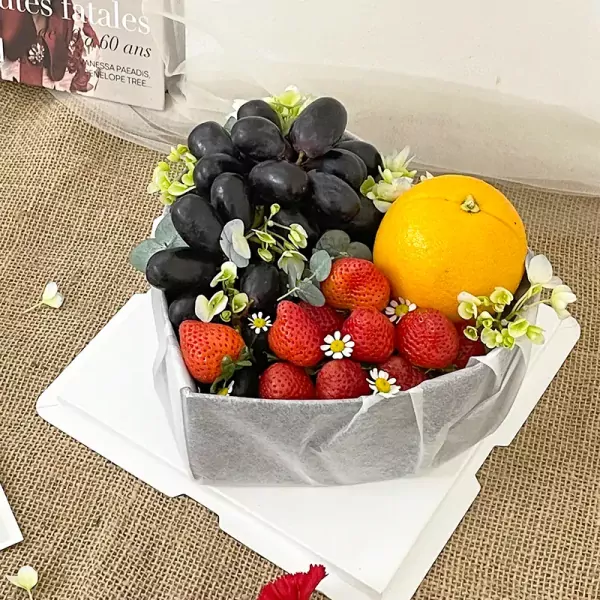 Fruit box with grapes, strawberries, and an orange, decorated with flowers and greenery.