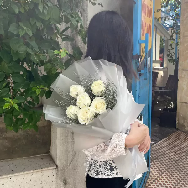 Woman in white lace top holding a bouquet of white roses.