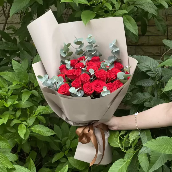Bouquet of 24 red roses with eucalyptus, wrapped in brown paper and tied with a ribbon.