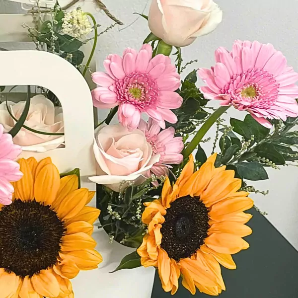 Bouquet of sunflowers, pink gerbera daisies, and light pink roses in a white basket.