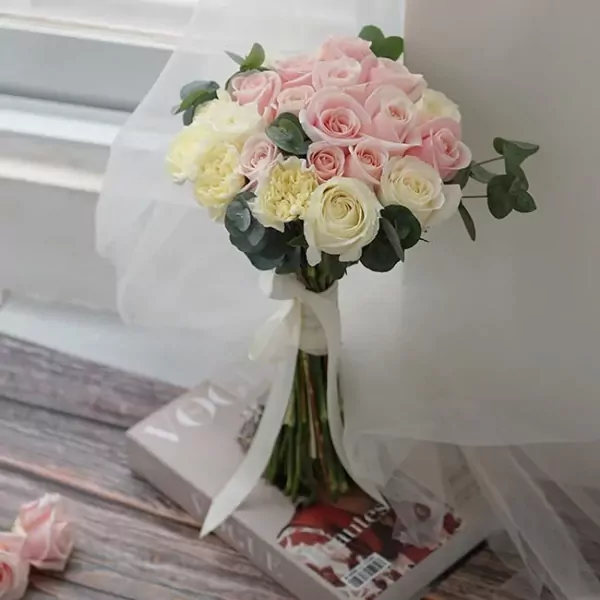 Pink and white roses and carnations in a bridal bouquet with a white ribbon.