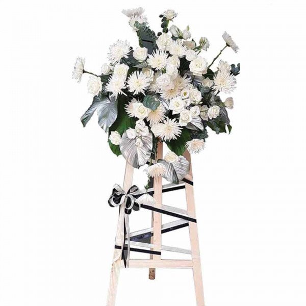 White funeral flower arrangement with roses and chrysanthemums on a wooden easel.