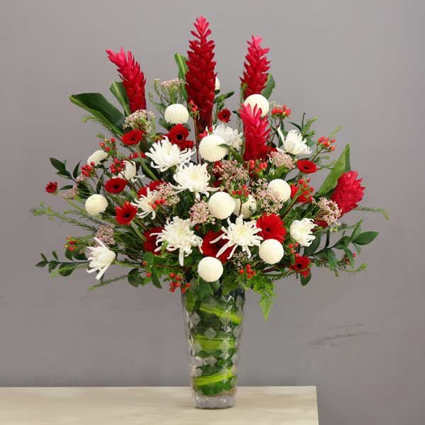 Large floral arrangement of red ginger, white chrysanthemums, and red gerbera daisies in a glass vase.