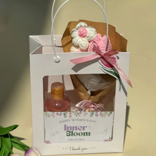 Gift bag with bottle of pink liquid, crochet tulip bouquet, and "Inner Bloom" card.