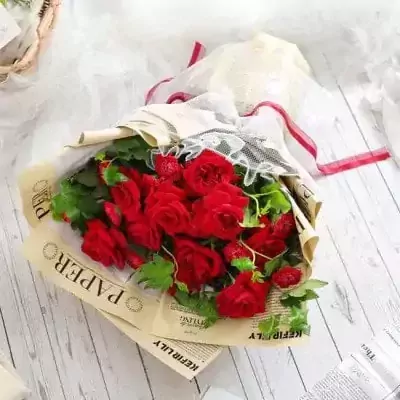 A bouquet of red roses and carnations with greenery, wrapped in newspaper and lace.