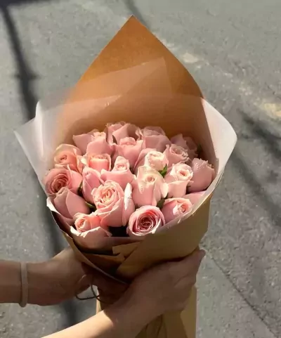 Bouquet of pink roses wrapped in brown paper and white tissue paper.