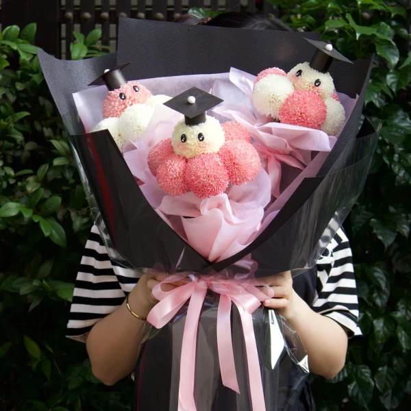 Graduation bouquet of white ping pong chrysanthemums and pink pom-poms, with graduation caps.