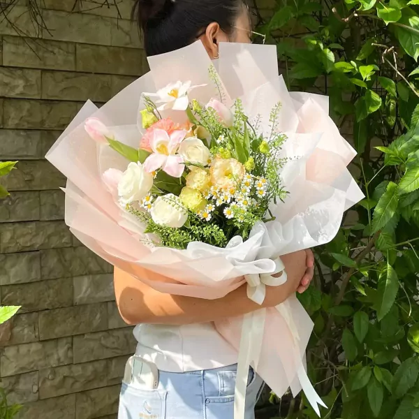 Woman holding a bouquet of white roses, pink tulips, and small white flowers.