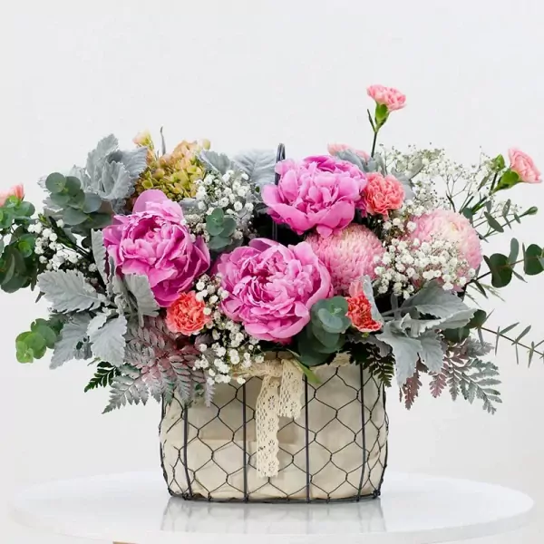 Pink peonies, chrysanthemums, and carnations in a wire basket with lace ribbon.