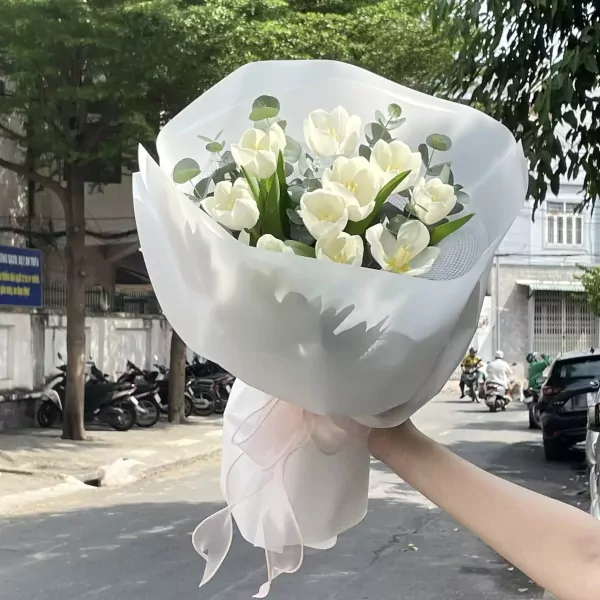 Bouquet of white tulips with eucalyptus, wrapped in white paper, tied with a sheer pink ribbon.