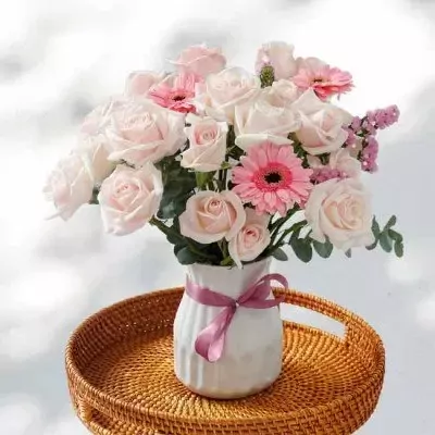 Bouquet of light pink roses and pink gerbera daisies in a white vase with a pink ribbon.