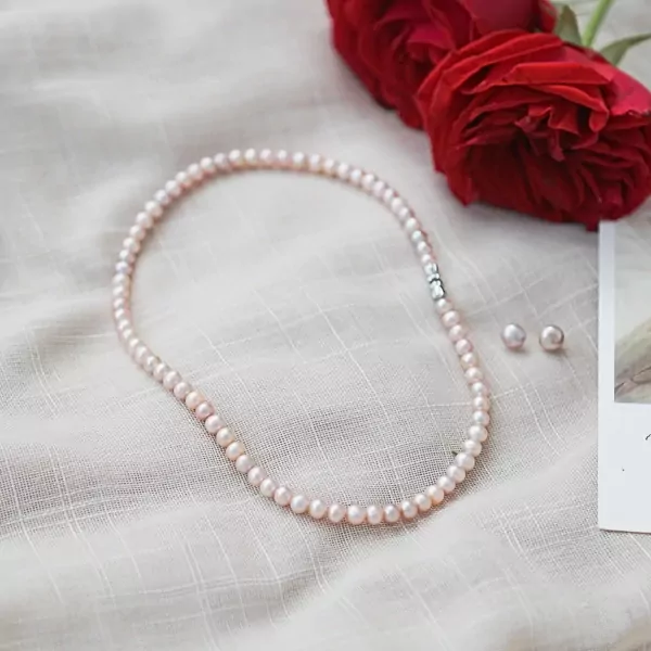 Pink pearl necklace and earrings on a white cloth with red roses.