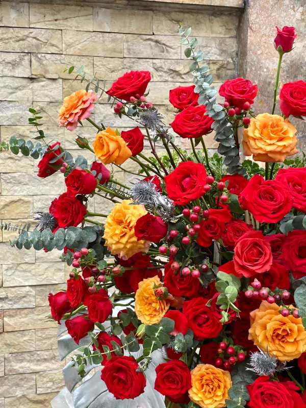 A large floral arrangement of red and orange roses with eucalyptus and red berries.