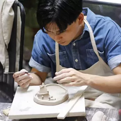 Person sculpting small clay houses with tools in a pottery workshop.