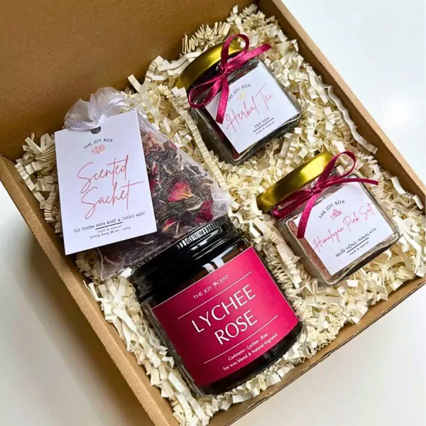 A gift box with a scented sachet, herbal tea, Himalayan pink salt, and a lychee rose candle.