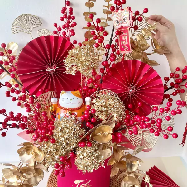 Maneki-neko cat with red and gold floral arrangement, featuring red paper fans.