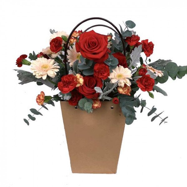 Red roses, white gerbera daisies, and red carnations in a brown paper bag flower arrangement.