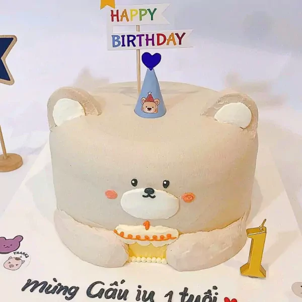 A cute bear-shaped birthday cake with "Happy Birthday" decorations and a "1" candle.
