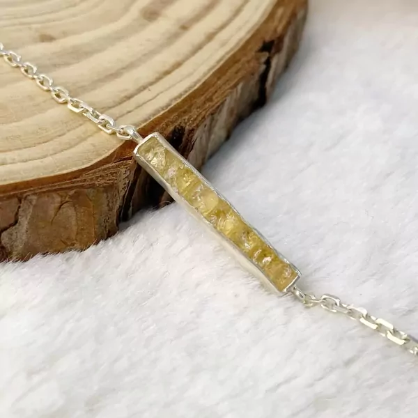 Silver bracelet with raw yellow gemstone bar pendant on a wooden surface.