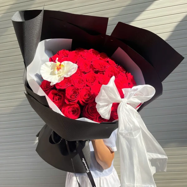 Bouquet of 50 red roses with a white orchid and a white ribbon, elegantly wrapped in black paper.