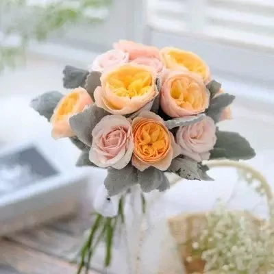 A bouquet of peach, pink, and yellow roses with dusty green foliage.