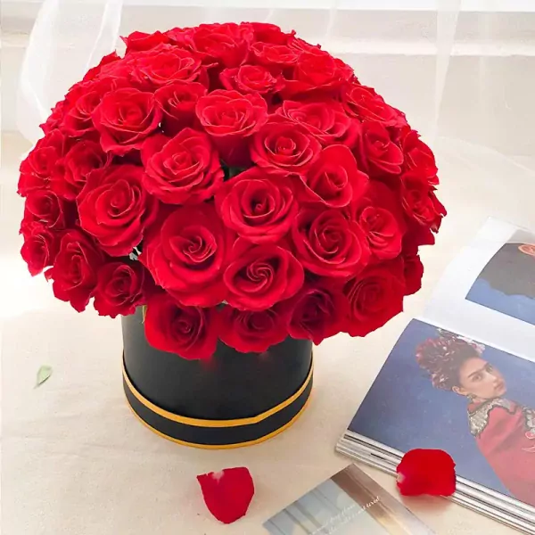 Round box of vibrant red roses with gold trim, next to an open magazine featuring Frida Kahlo.
