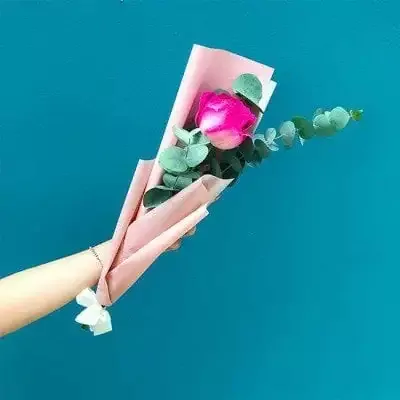 Pink rose with eucalyptus in pink paper, held by an arm with a bracelet.