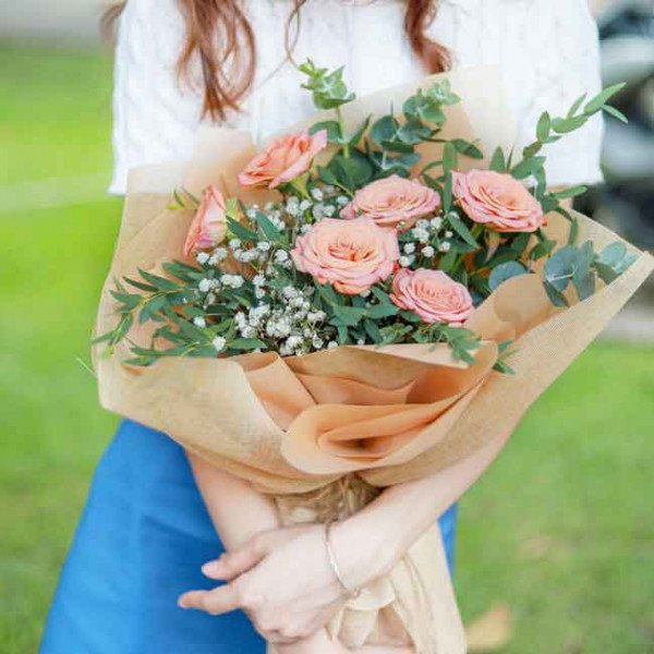 Bouquet of peach roses and baby's breath wrapped in brown paper.