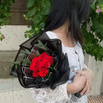 Bouquet of red roses in black wrapping, held by a person in a white lace top.