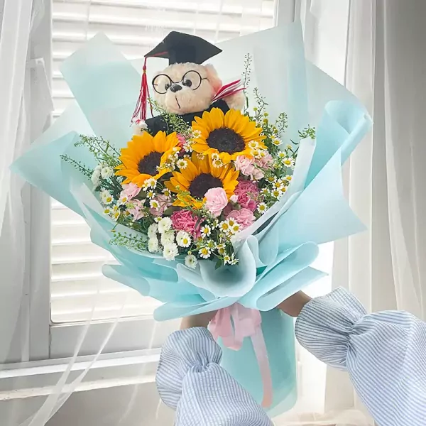 Graduation bouquet with sunflowers, carnations, daisies, and a teddy bear wearing a cap.