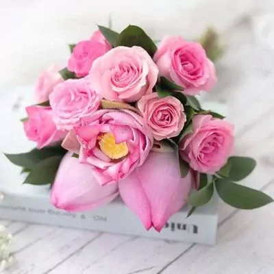 Pink lotus and rose bouquet with green leaves, resting on a book.