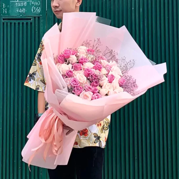 Man holding a large bouquet of pink and white roses wrapped in pale pink paper.