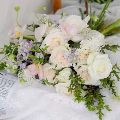 A bridal bouquet of white roses, pink tulips, and delicate filler flowers on a white lace cloth.