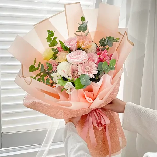 A bouquet of pink and white flowers wrapped in peach paper with a pink ribbon.