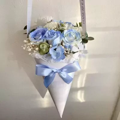 A pastel blue and white floral bouquet in a white cone with a blue ribbon.