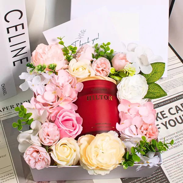 A red Hilton candle surrounded by pink and white flowers in a gift box.