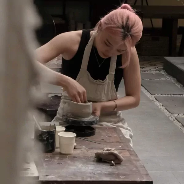 Person with pink hair working on a pottery wheel at a workshop.