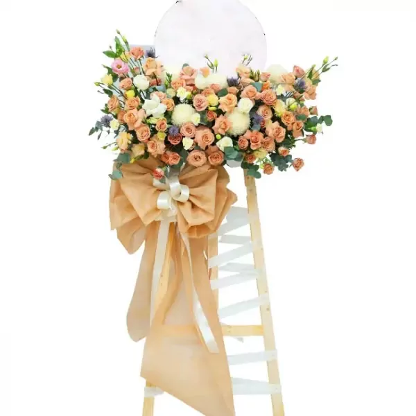 A tall bouquet of peach and white roses, chrysanthemums, and other flowers on a wooden stand with a large peach bow.